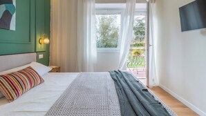 A bedroom with a bed, a bedside table, a TV mounted on the wall, and a window with curtains.