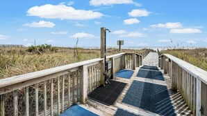Un paseo marítimo de madera que conduce a una playa, con cielo despejado y nubes.