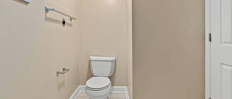 A small, clean bathroom with a toilet, a towel rack, and a framed picture on the wall.