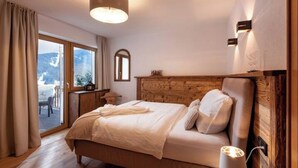 Un dormitorio con cabecera de madera, una cama grande con ropa blanca, una lámpara de noche y vistas al exterior a través de un ventanal corredero.