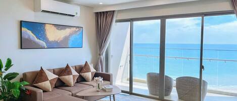A modern living room with a sofa, coffee table, and a large window overlooking the sea.