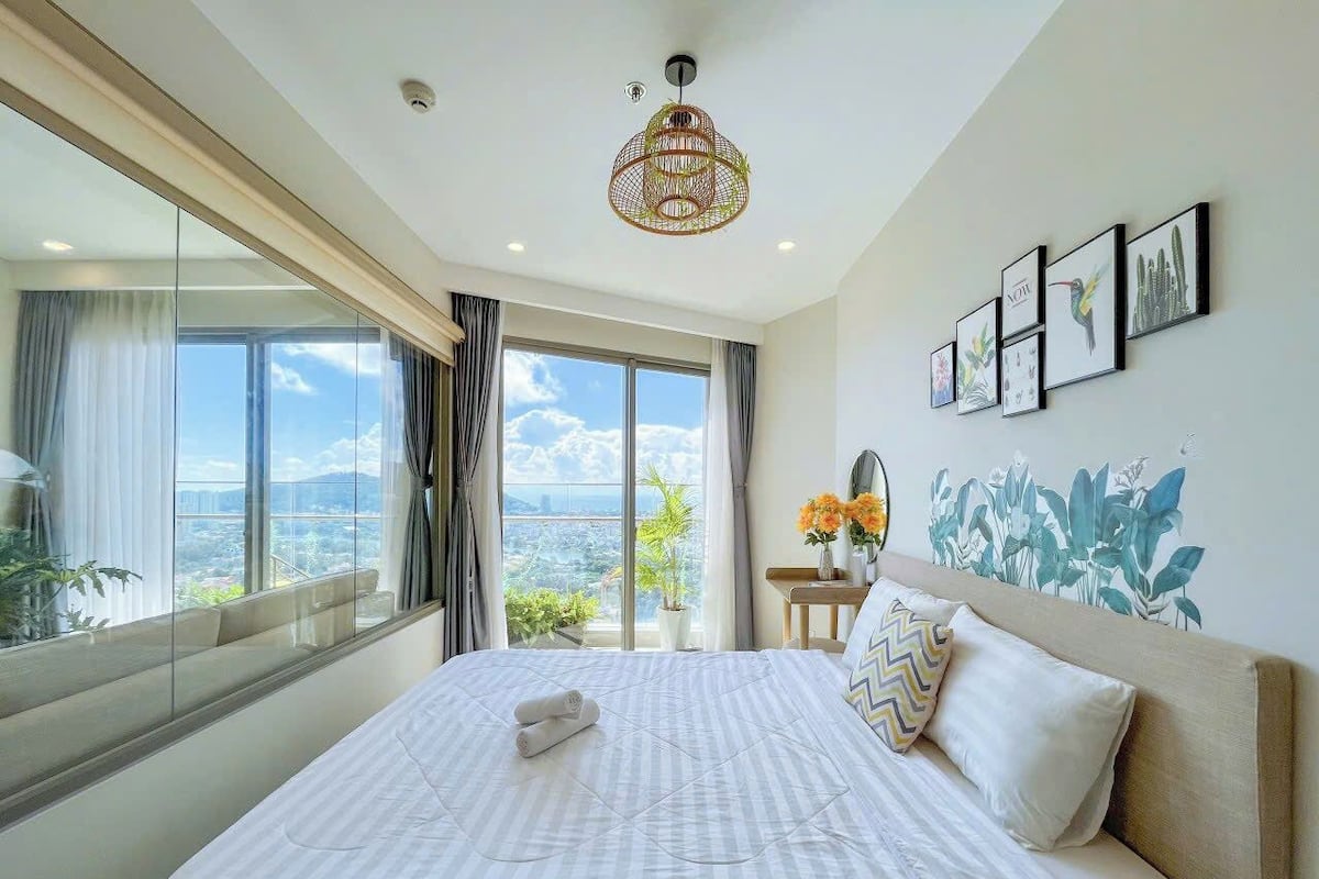 Habitación de hotel con una cama grande, vistas a la ciudad y un balcón con plantas.