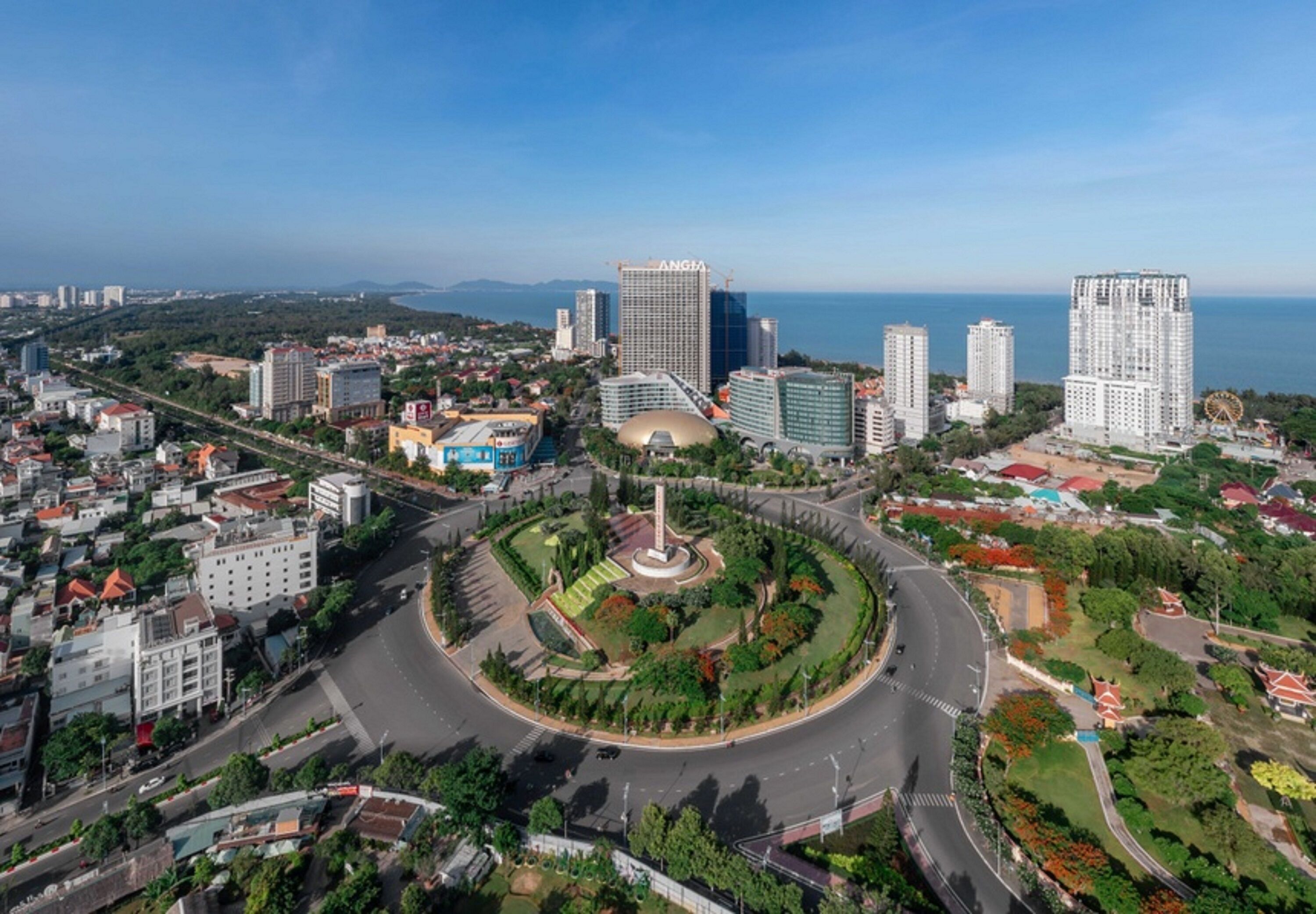 Panorama urbano con una rotatoria, edifici moderni e un corpo d'acqua sullo sfondo.