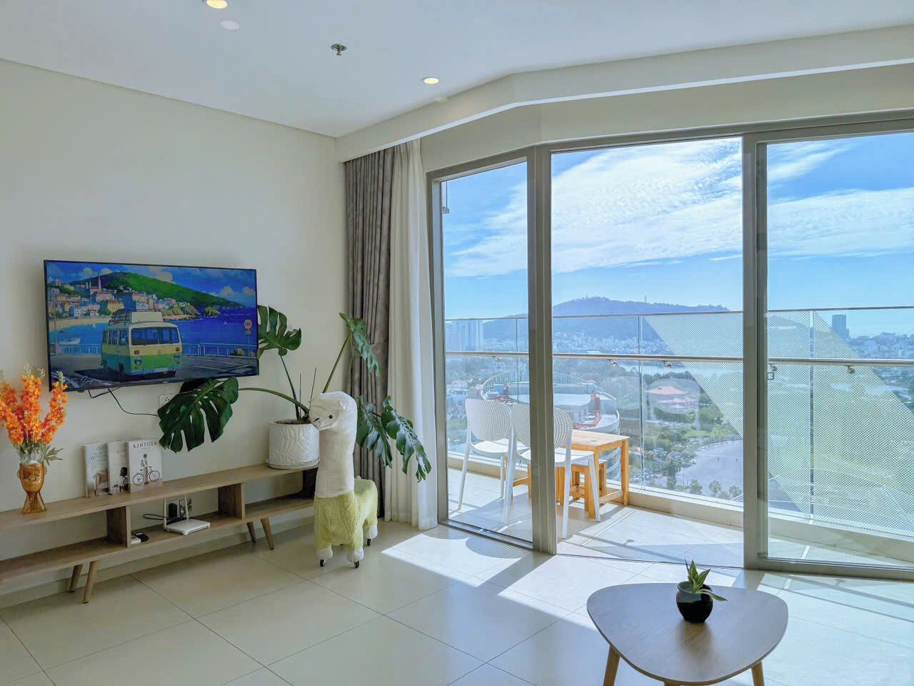 A modern living room with a large TV, a balcony with a view of the city, and a dining area.