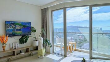 Uma sala de estar moderna com uma televisão grande, uma varanda com vista para a cidade e um espaço de jantar.