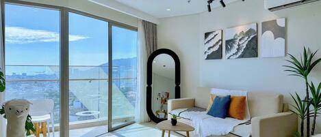 A modern living room with a large sliding glass door leading to a balcony, a sofa, a coffee table, and a mirror.