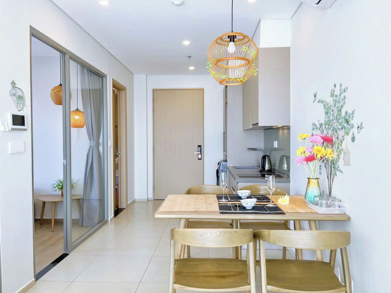 A modern dining area with a glass partition, wooden chairs, a table set for two, and a hanging light fixture.