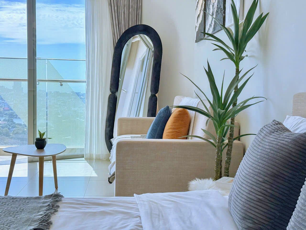 A modern living room with a large window, a sofa, a chair, and a small table with a plant.