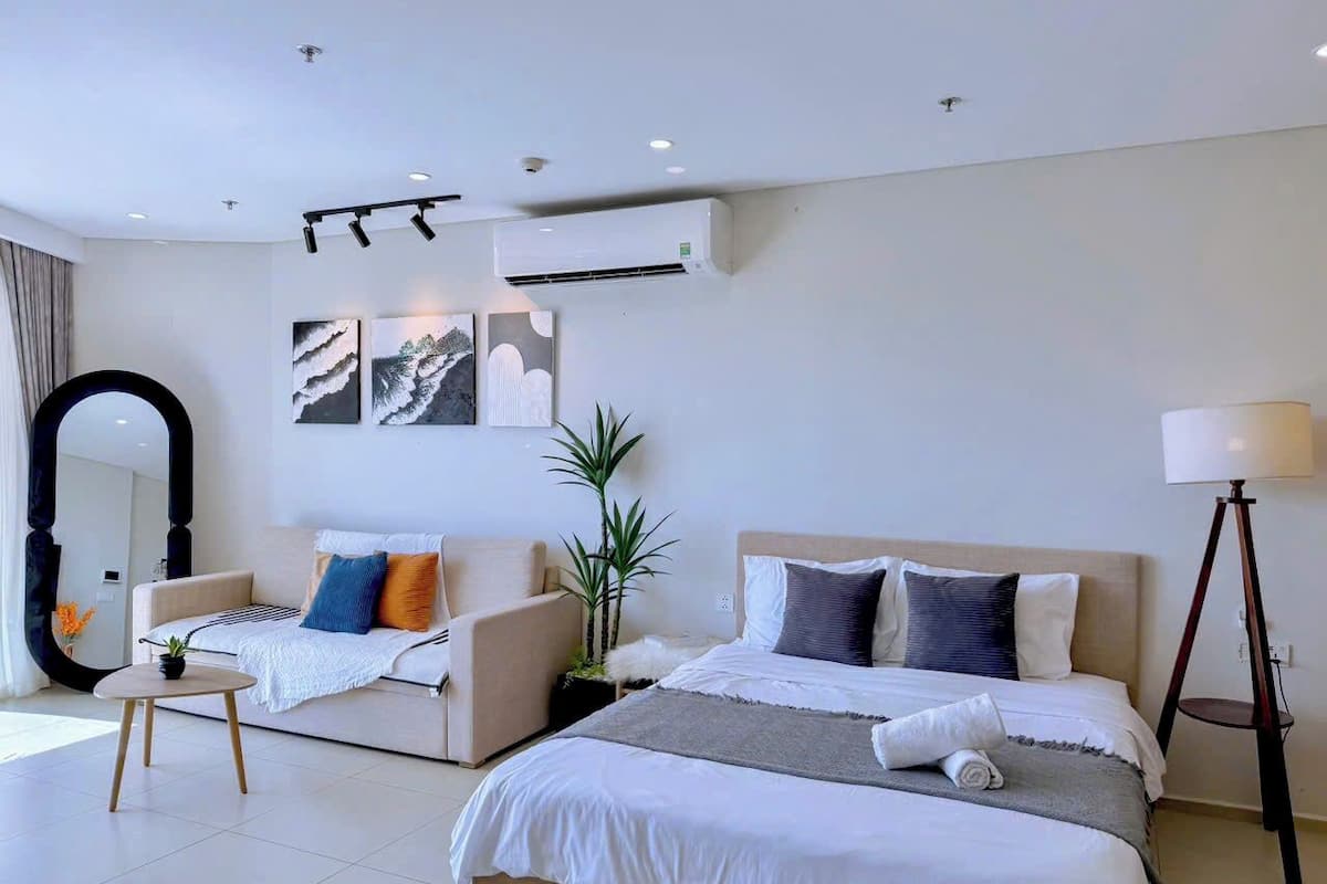 Una habitación de hotel moderna con una cama grande, un sofá, una mesita y un espejo.
