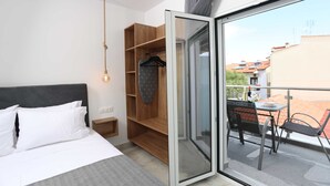 Un dormitorio con cama, armario de madera, ropa colgada y balcón con mesa y sillas.
