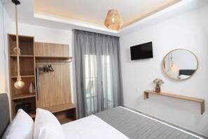 A modern hotel room with a bed, a wooden wardrobe, a TV, a mirror, and a hanging light fixture. - Gregory Luxury Apartments  (Kassandra)