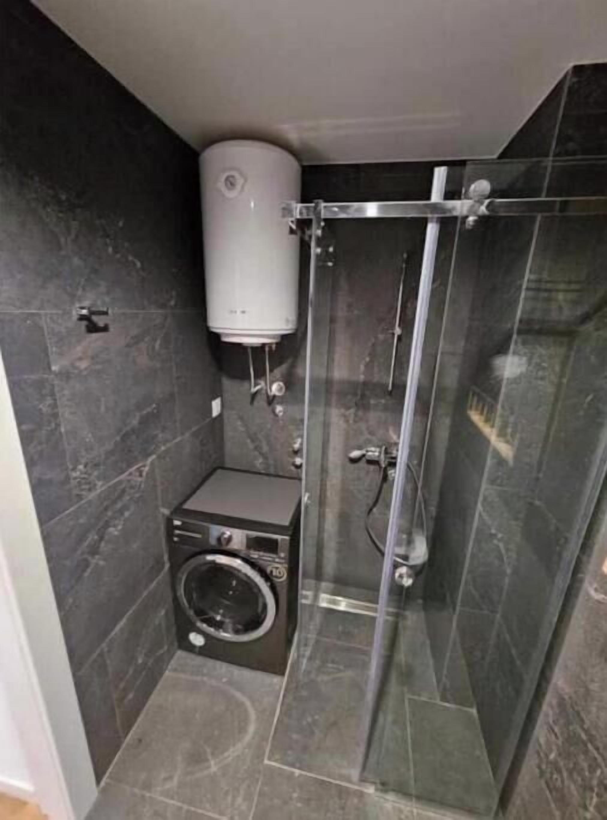 A compact bathroom with a washing machine, a glass shower enclosure, and a water heater.