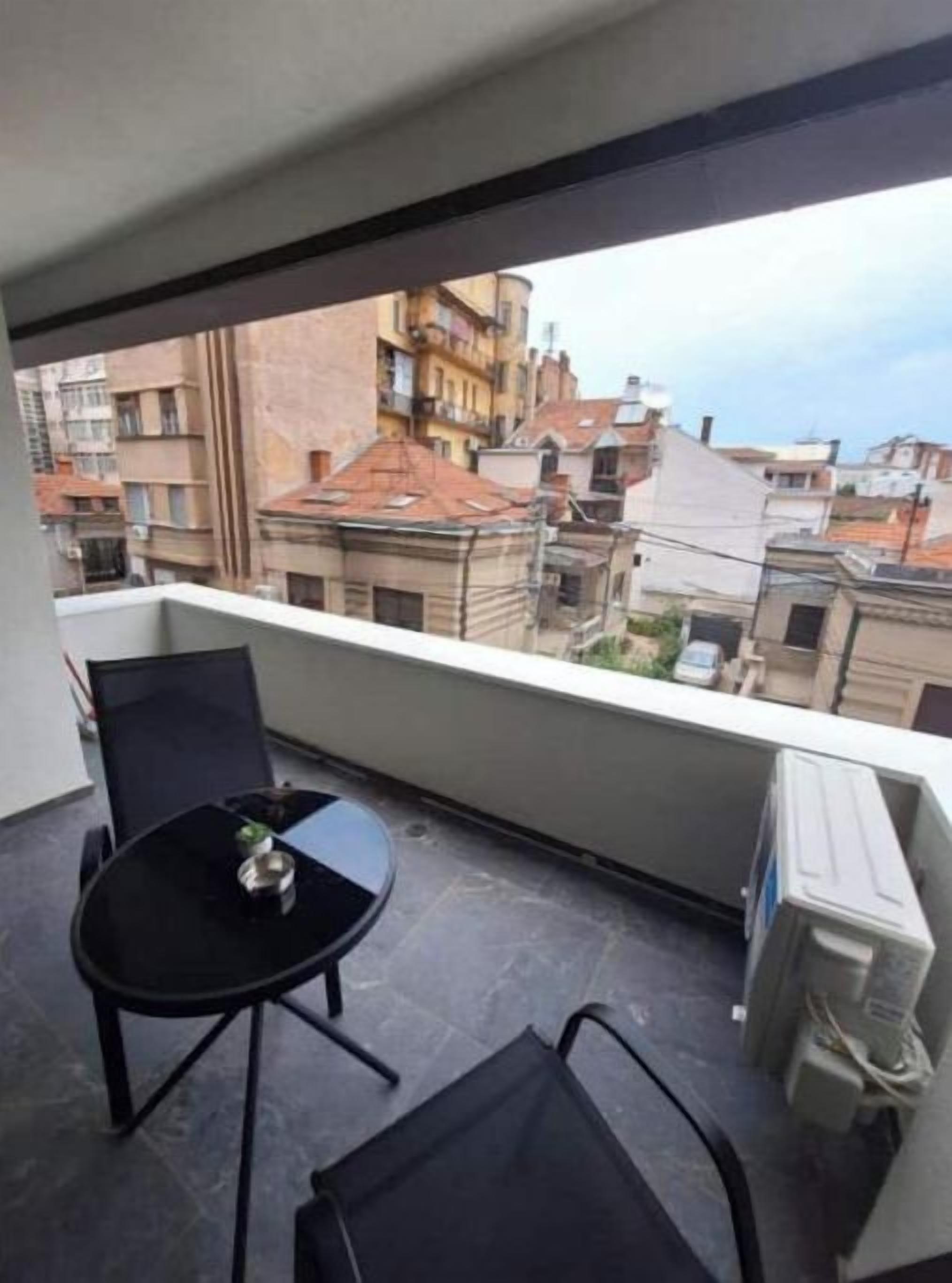 A balcony with a table and chairs, overlooking a residential area with buildings.