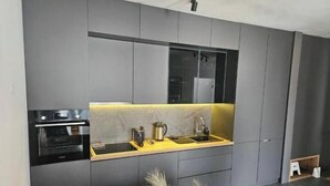 Een moderne keuken met grijze kastjes, een zwarte oven, een geel aanrecht en een roestvrijstalen spoelbak.