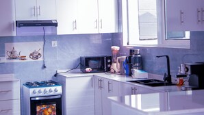 A modern kitchen with white cabinets, a built-in oven, a microwave, and a large window providing natural light. - THE TREKKER'S REST LODGE (Cyuve)