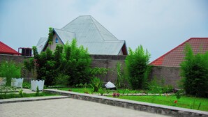 A building with a peaked roof, surrounded by a landscaped garden with various plants and a paved walkway. - THE TREKKER'S REST LODGE (Cyuve)