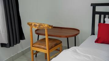 A room with a bed, a wooden chair with a leather seat, a small wooden table, and a red pillow on the bed.
