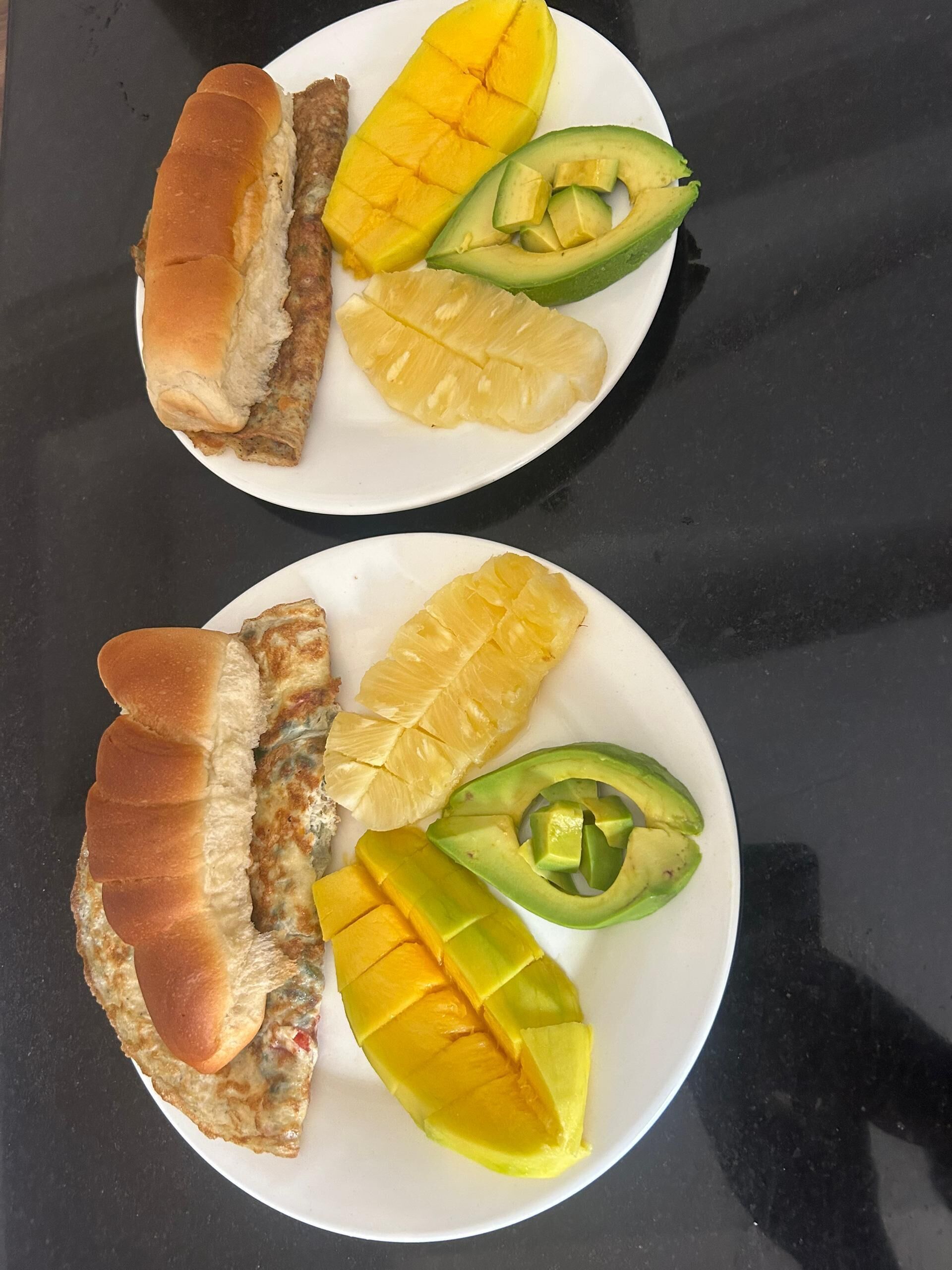 Two plates with fried fish, mango, and avocado.