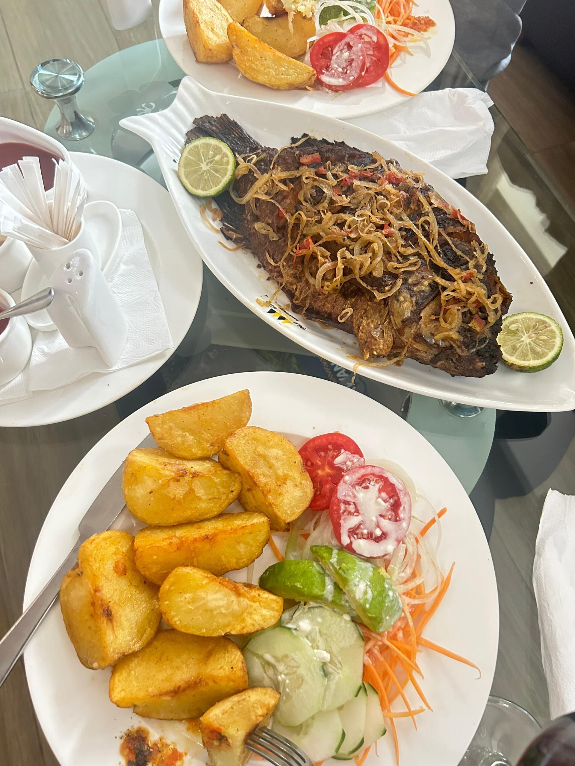 Una mesa de comedor con platos de comida, incluyendo patatas fritas, un plato de pescado y una ensalada.