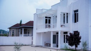 A two-story residential building with a balcony on the upper floor, a covered patio area, and a small garden with plants and flowers. - THE TREKKER'S REST LODGE (Cyuve)