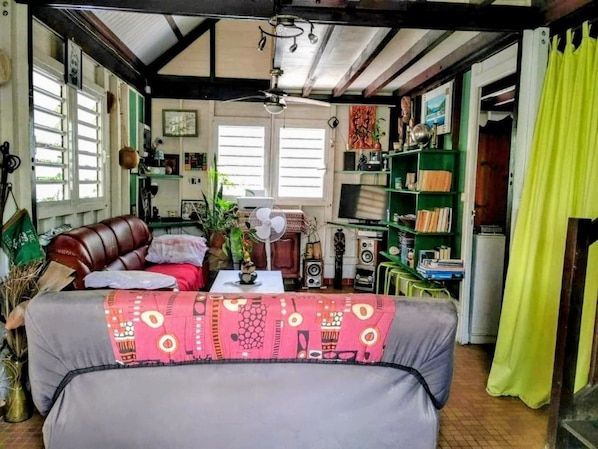 A cozy living room with a sofa, a fan, and a bookshelf.