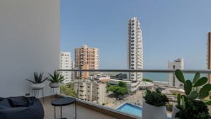 A balcony with a view of a cityscape, including a tall building and a swimming pool.