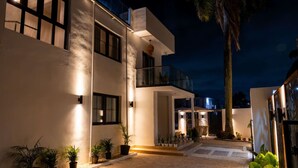 A modern building with a paved courtyard, potted plants, and a balcony overlooking the area.