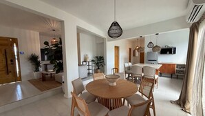 A spacious living area with a round wooden table and chairs, a kitchen in the background, and a dining area with a large window. - Couple`s King Suite at Ocean Park Beach Club (San Juan)