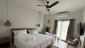 A bedroom with a large bed, a ceiling fan, a TV, and a window with curtains.