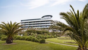 A modern multi-story hotel with a curved rooftop, surrounded by well-maintained gardens and palm trees. - 24 The Liner sits so close to the cove that the fresh sea breeze flows in through the windows. (Falmouth)