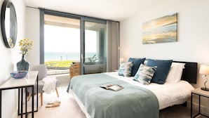 A bedroom with a bed, a desk, a chair, a vase with flowers, and a view of the sea. - 24 The Liner sits so close to the cove that the fresh sea breeze flows in through the windows. (Falmouth)