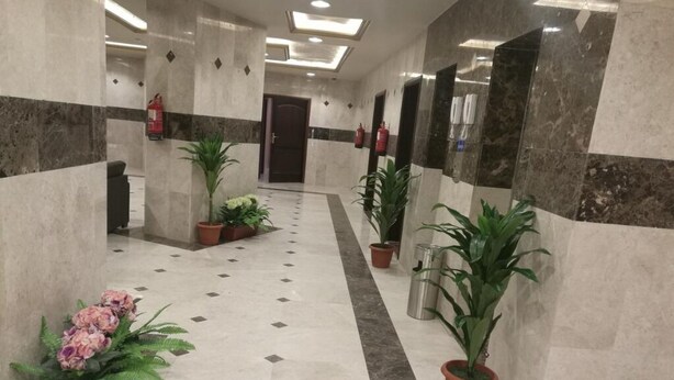 Een hotel lobby met een marmeren vloer, potplanten en een brandblusser.
