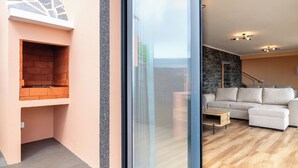 A modern living space with a glass door leading to an outdoor area, a built-in brick fireplace, a stone accent wall, a white sectional sofa, and a wooden coffee table.