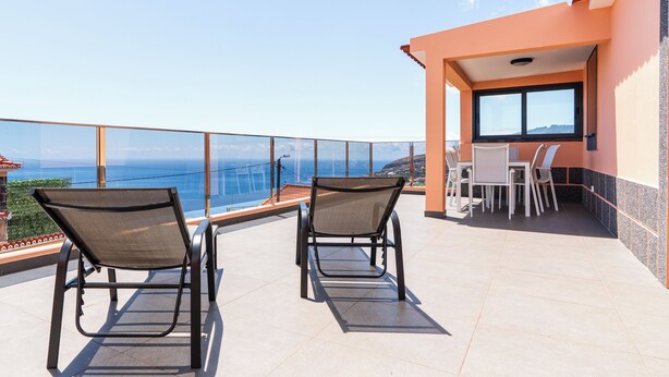 A balcony with two chairs and a table, overlooking a scenic view of the ocean.