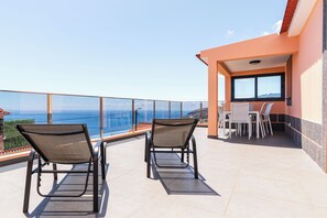 A balcony with two chairs and a table, overlooking a scenic view of the ocean. - Sunset House II (Arco da Calheta)