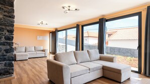 A modern living room with a sectional sofa, a stone accent wall, large windows, and a ceiling light fixture.