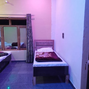 Una habitación pequeña y con poca luz, con dos camas individuales, una ventana con cortinas y un ventilador de techo.