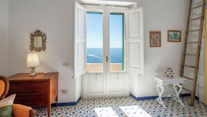 Ein Zimmer mit Nachttisch aus Holz, einer Lampe, einem weißen Tisch mit einer Vase, einer Holzleiter und einer Tür mit Blick auf das Meer.