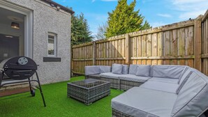 A patio with a sectional sofa, a grill, and artificial grass. - Arran Cottage Spacious 4-Bedroom House (Coatbridge)