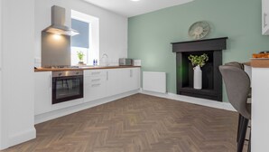 A modern kitchen with white cabinets, a built-in oven, and a wooden countertop. - Arran Cottage Spacious 4-Bedroom House (Coatbridge)