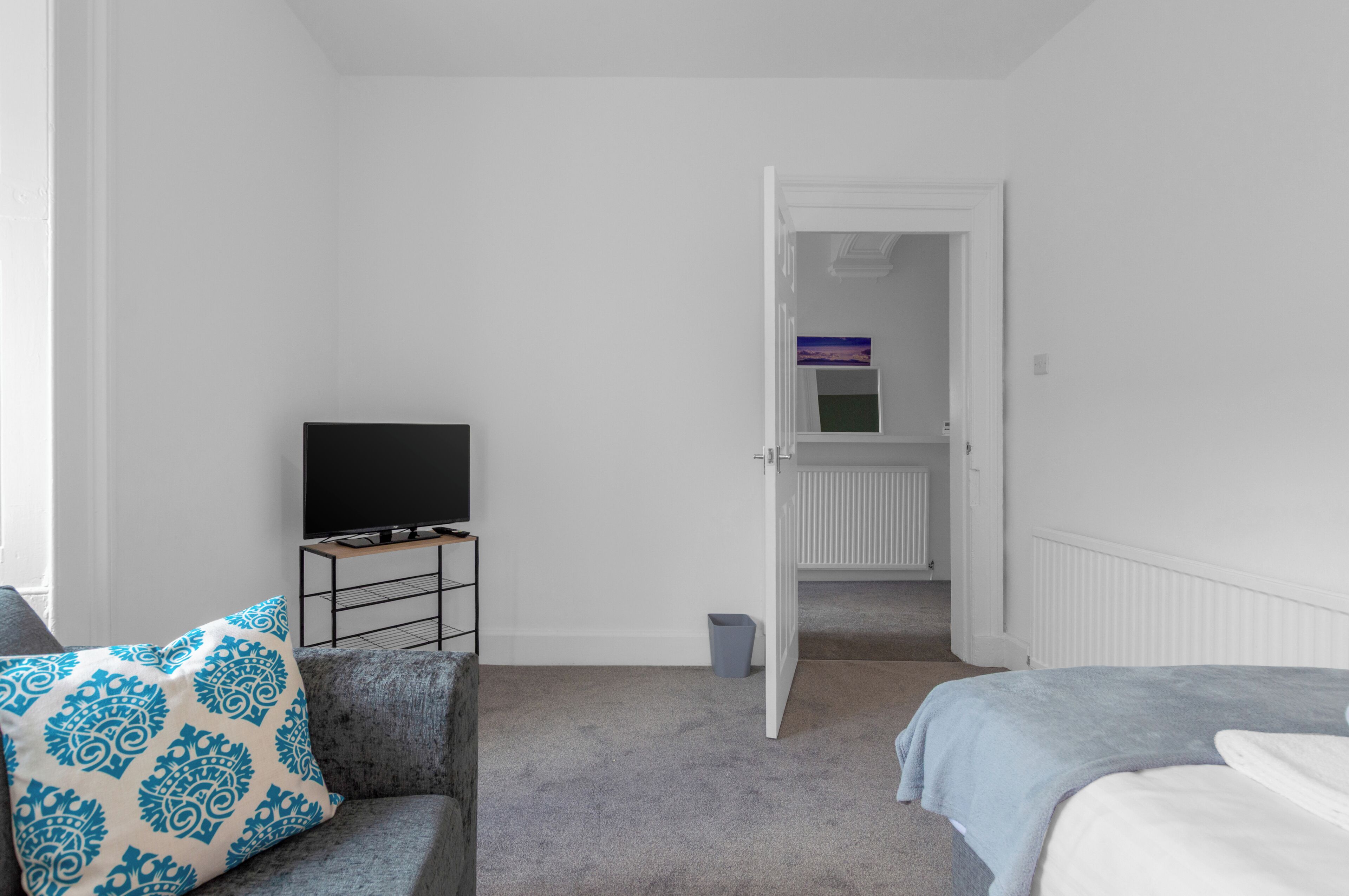 Ein Schlafzimmer mit einem Bett, einem Fernseher auf einem Schrank, einem grauen Sofa und einer Tür zu einem Badezimmer.