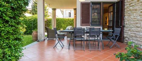 A covered patio with a table and chairs, a grill, and a stone wall.