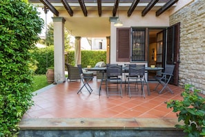 Un patio couvert avec une table et des chaises, un barbecue et un mur en pierre.