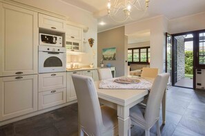 A kitchen with white cabinetry, a dining table with chairs, and a view of the outdoors through a glass door.