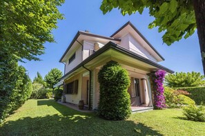 Een tweelaags huis met een overdekte veranda, een verzorgd gazon en omliggend groen.