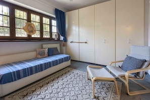 A room with a sofa, a chair, a patterned rug, a wardrobe, and a window with curtains.