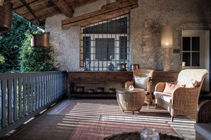 A rustic patio with wicker furniture, a wooden bench, and a view of greenery through a barred window.