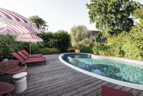 En træterrasse med swimmingpool, liggestole og stribede parasoller.