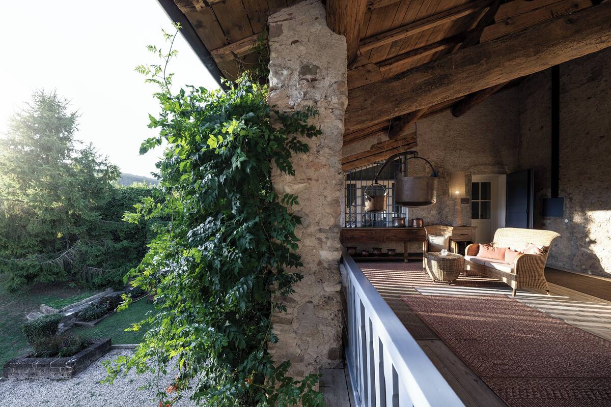 Un balcon en bois rustique, agrémenté d’un mur en pierre, d’un canapé en osier et d’un pot suspendu.
