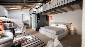 A bedroom with a large bed, a desk, and a chair. There is a staircase leading to an upper level.